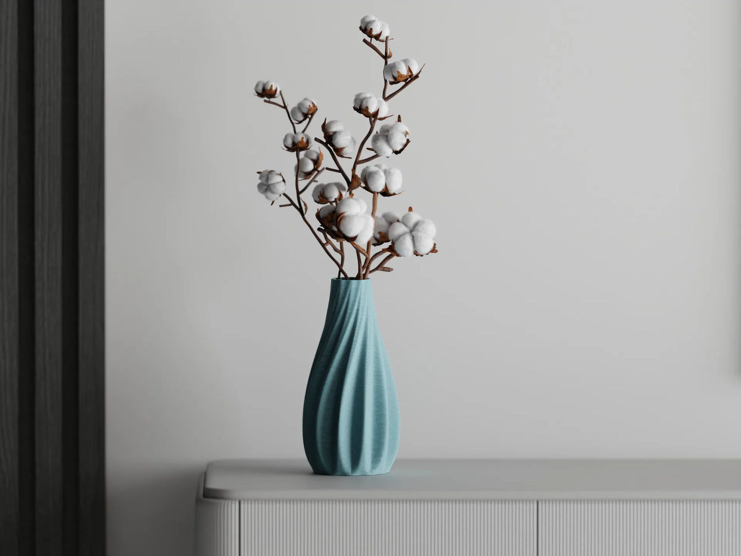 3D printed ocean blue vase with cotton branches, displayed on a white cabinet against a light gray wall