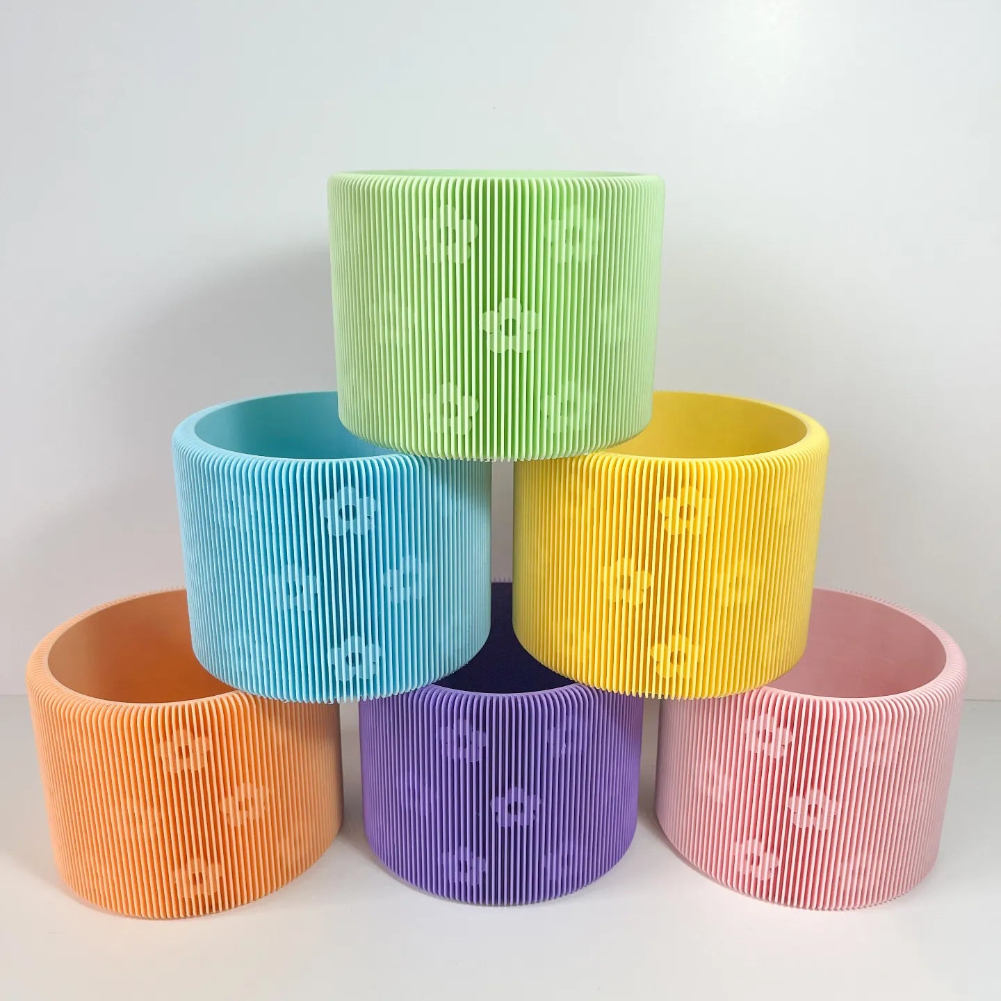 Stack of rainbow-colored ribbed flower pots with floral patterns on a white background