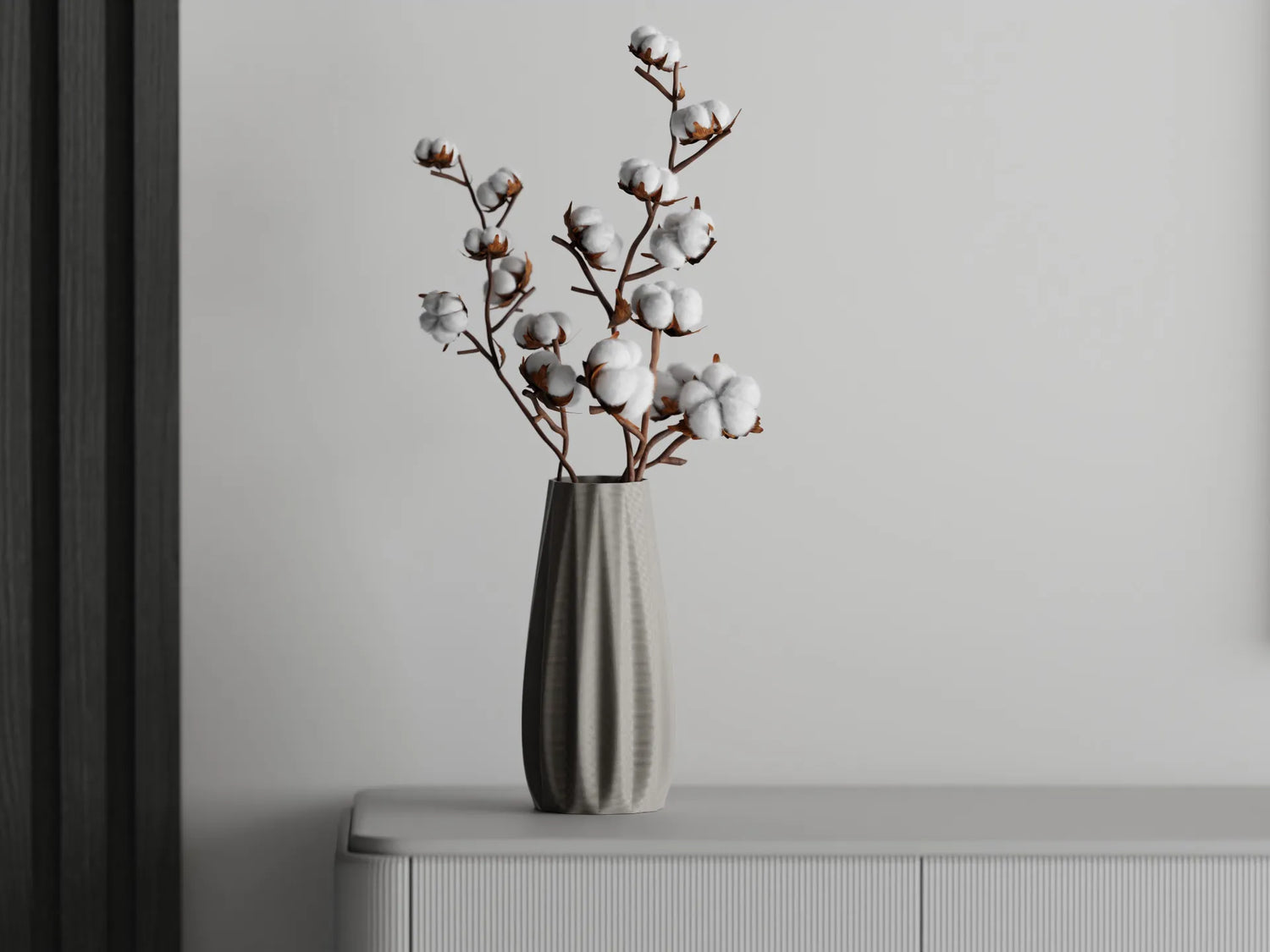 Tall ribbed vase with white cotton branches displayed on a light gray cabinet against a soft gray wall